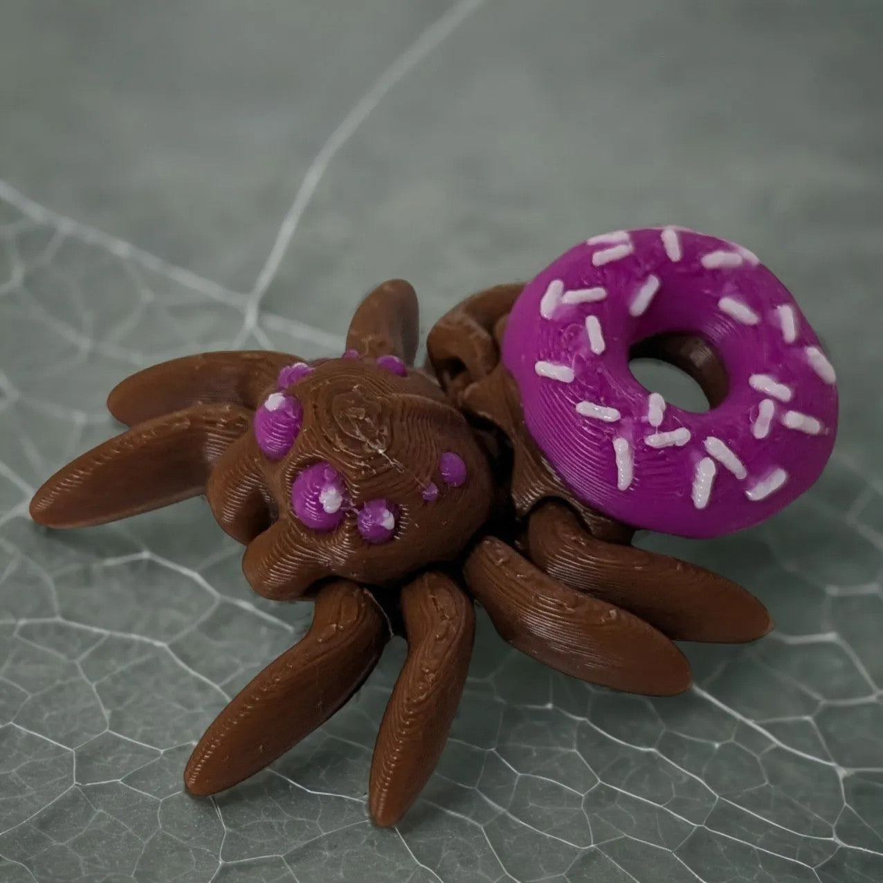 Mehrfarbige, flexible 3D-gedruckte Donutspinne mit leckerem bunten Donut auf dem Rücken