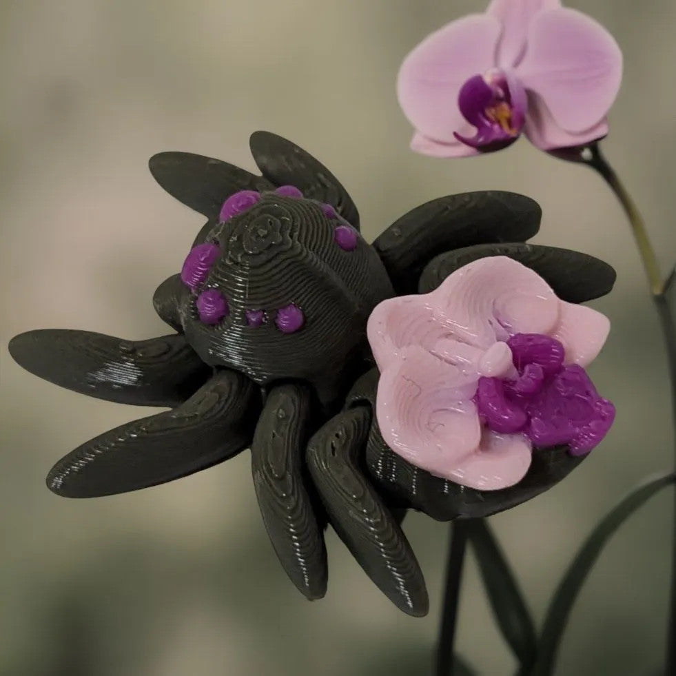 Mehrfarbige, flexible 3D-gedruckte Orchideenspinne mit Orchidee in Rosa und Magenta dem Rücken.