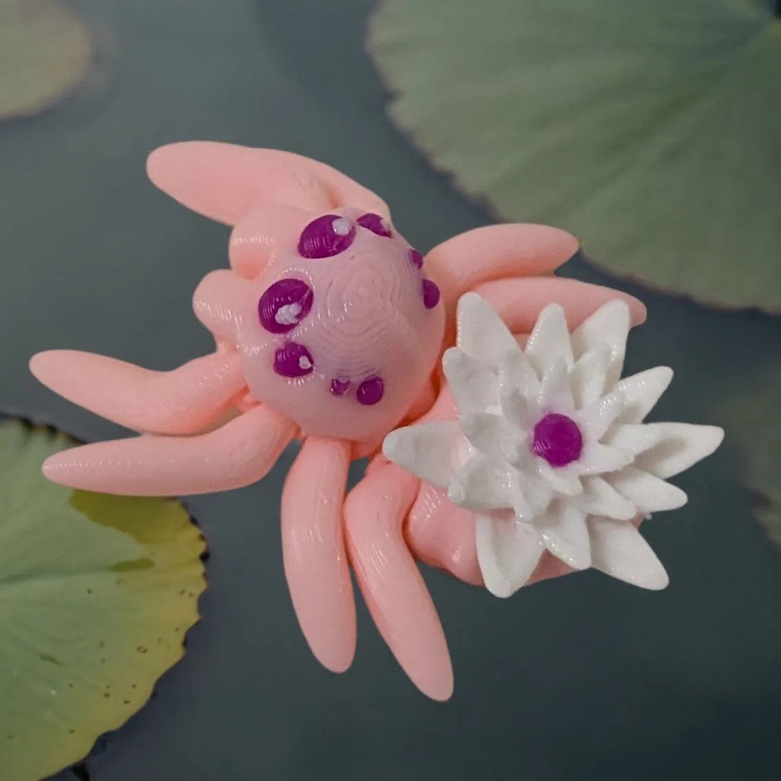 Mehrfarbige, flexible 3D-gedruckte Lillienspinne mit Wasserlilie dem Rücken. Rosa mit Lilie in weiss